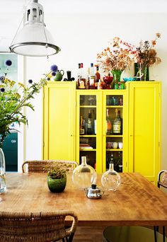 a dining room table with vases and bottles on it's shelves next to a yellow cabinet