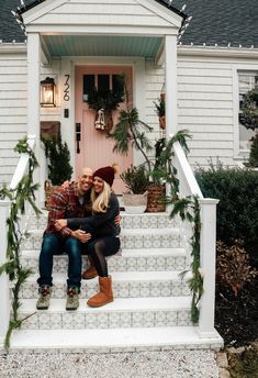 a man and woman sitting on steps in front of a house with christmas wreaths