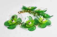 a green bracelet with flowers and pearls hanging from it's side on a white surface