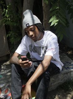 a young man sitting on the ground looking at his cell phone