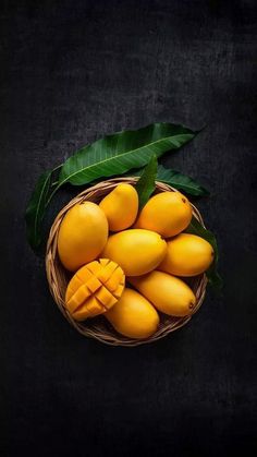 a basket filled with mangoes next to a green leaf