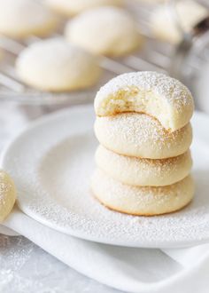 a stack of powdered sugar cookies sitting on top of a white plate next to other pastries