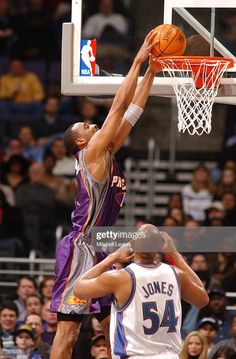 a basketball player dunking the ball in front of an opponent during a game with spectators watching