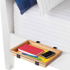 a wooden tray with two notebooks and a phone on it next to a bed