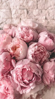 a bouquet of pink peonies in front of a brick wall