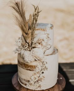 a wedding cake decorated with dried flowers and feathers