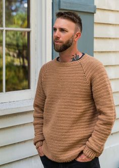 a man standing in front of a window wearing a brown sweater