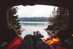 a person laying on top of a blanket in the back of a car next to a lake