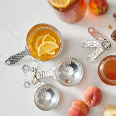 there are many different types of drinks on the table with spoons and fruit around them