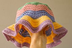 a woman's hand holding up a multicolored crocheted sunhat