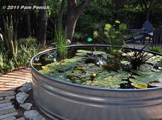 a large metal tub filled with water lilies in a garden area next to a patio