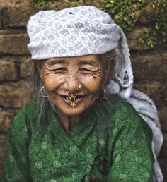 an old woman with her eyes closed and nose piercing in front of a brick wall