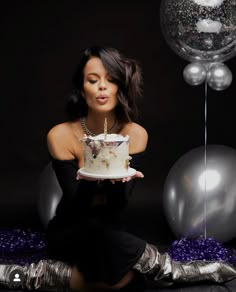 a woman sitting on the floor with a cake in front of her and balloons behind her