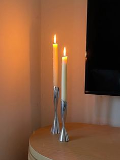 two lit candles sitting on top of a table next to a flat screen tv in a room