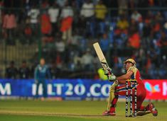 a man holding a cricket bat on top of a field next to another person wearing red and yellow