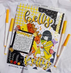 an open book with yellow markers and writing on the cover, next to some pens