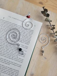 an open book with some metal items on top of it next to flowers and beads