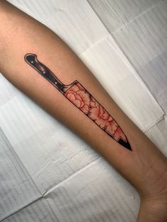 a knife tattoo on the arm with red and black flowers in it's blade