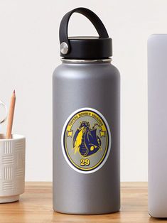 a silver water bottle with a black lid and a white cup next to it on a wooden table