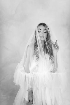 a woman wearing a veil and holding her hands up in the air while posing for a black and white photo