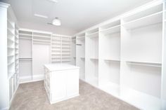 an empty walk in closet with white shelving and cabinets on the walls, carpeted floor