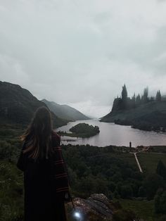 a woman standing on top of a lush green hillside next to a large body of water