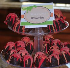 chocolate brownies with red icing are on a cake platter, and there is a sign that says volcano brownies