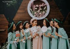 a group of women standing next to each other in front of a wooden sign with flowers on it