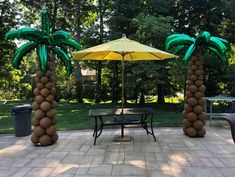 two palm trees made out of balloons sitting in the middle of a patio with tables and chairs