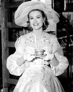 a woman in a dress and hat holding a cup with her hands on the plate