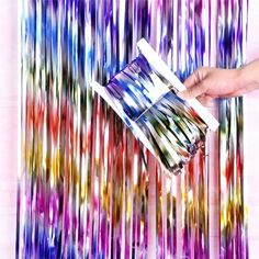 a person is holding a box in front of a multicolored background that looks like streamers