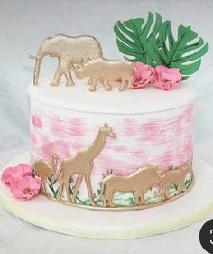 a pink and white cake with gold animal decorations on it's top, surrounded by flowers