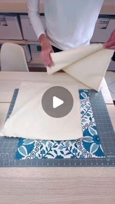 a person is making a quilt on top of a table with a piece of cloth