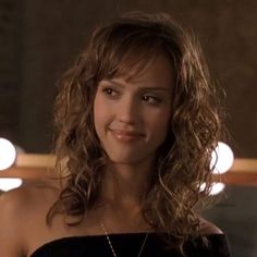 a beautiful young woman in a black dress smiling at the camera with lights behind her