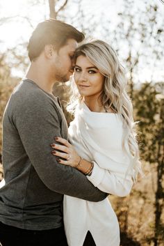 a man and woman embracing each other in front of some trees with the sun shining on them