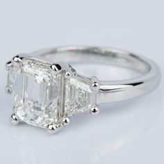 an emerald cut diamond ring with three baguets on the sides and four clawed shoulders