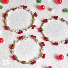 three bracelets with red and green beads on a white tablecloth next to leaves