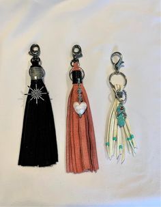 three tasseled keychains with charms attached to them on a white surface