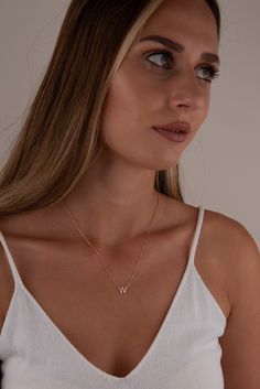 a woman wearing a white tank top and gold necklace with the letter v on it