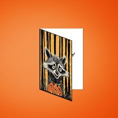 a raccoon is peeking out from behind a halloween card on an orange background