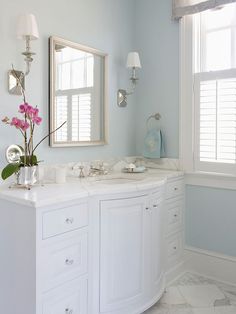 a white bathroom with two sinks and large mirrors on the wall above them is decorated with pink flowers