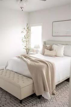 a white bedroom with a bed, ottoman and ceiling fan in the corner next to it