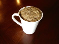 a white cup filled with oatmeal sitting on top of a wooden table