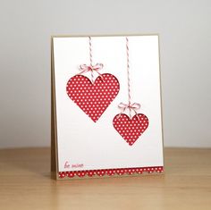 two red hearts hanging from strings on a white card