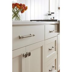 a vase with flowers sitting on top of a kitchen counter next to a sink and cabinets