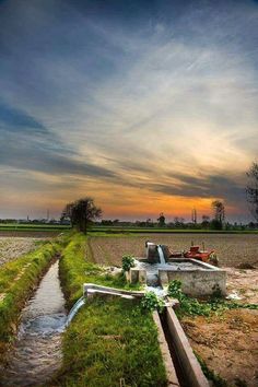 a small stream running through a field next to a large farm with tractor trailers in the distance