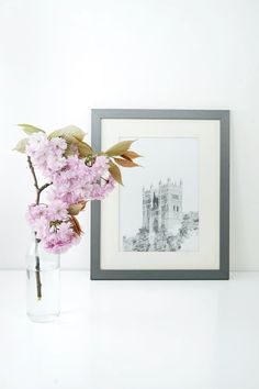 a vase with pink flowers in it next to a framed photograph on a white table