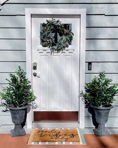 two potted plants are sitting on the front step of a house with a welcome mat