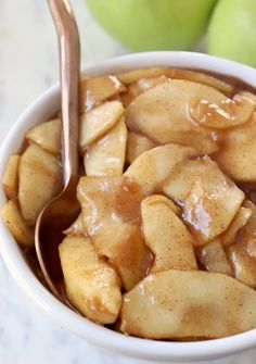 a bowl filled with apple slices covered in caramel sauce next to two green apples