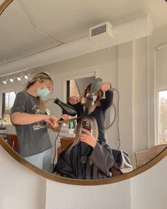 a woman is blow drying her hair in front of a mirror while another woman watches